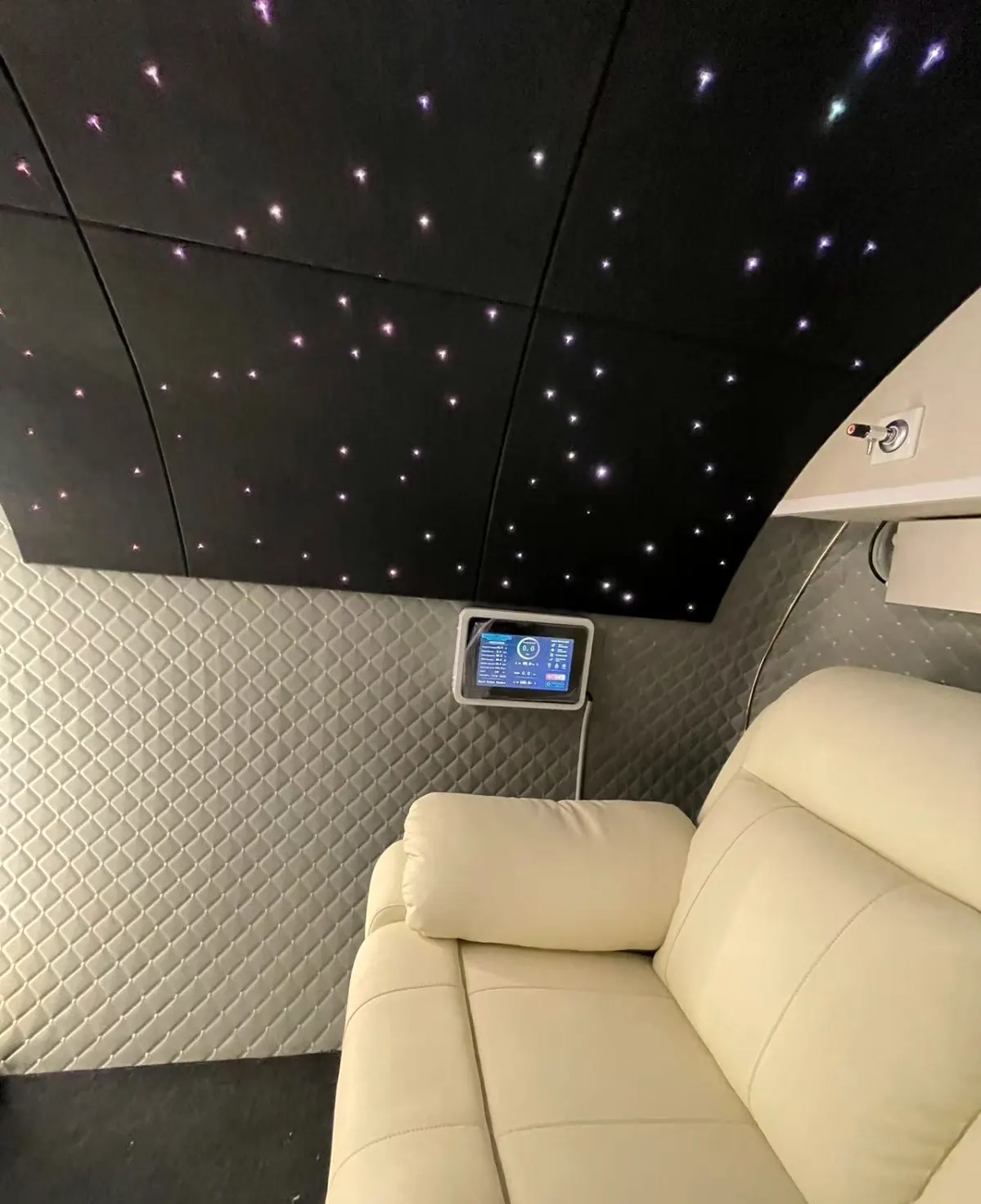 Ivory recliner beside quilted grey walls, internal control screen and starlight ceiling